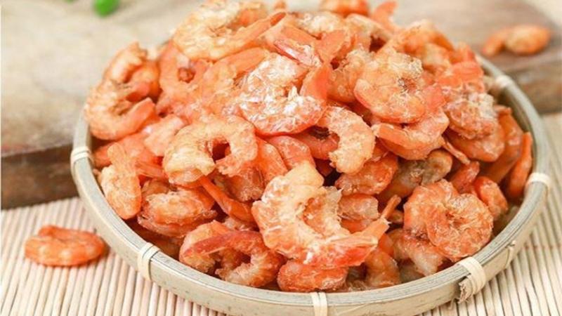 Giỏ đựng đầy tôm khô màu cam, đặt trên bề mặt tre, tạo cảm giác ấm áp và mộc mạc.